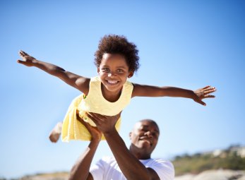 Helping his daughter soar! A father lifting his adorable daughter into the air while enjoying a day at the beach